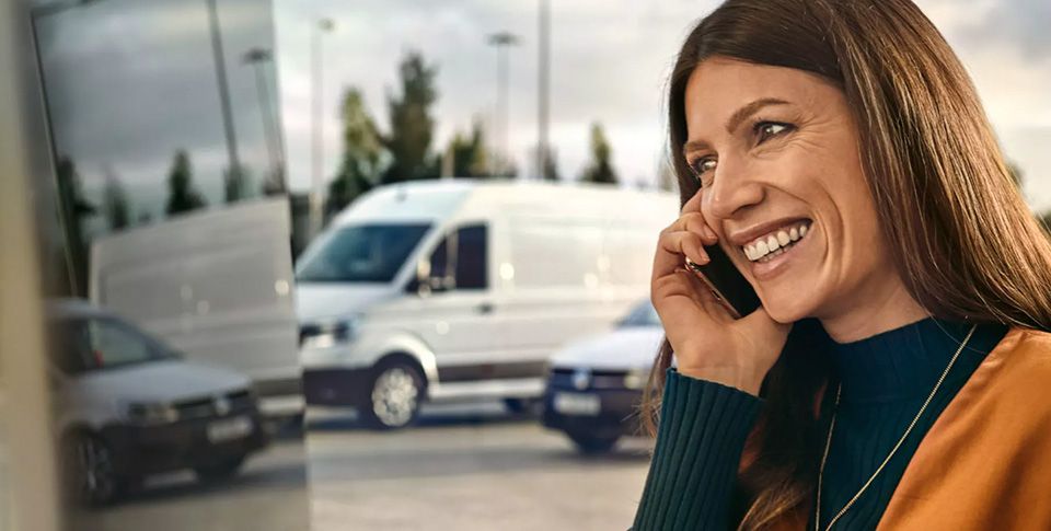 Eine Frau telefoniert und lächelt dabei. Im Hintergrund: zwei VW Nutzfahrzeuge.