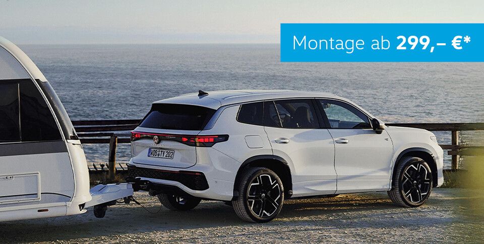 Volkswagen Tayron in Wei&szlig; mit Wohnwagen an Anh&auml;ngevorrichtung vor Meer. St&ouml;rer: Montage ab 299 &euro;