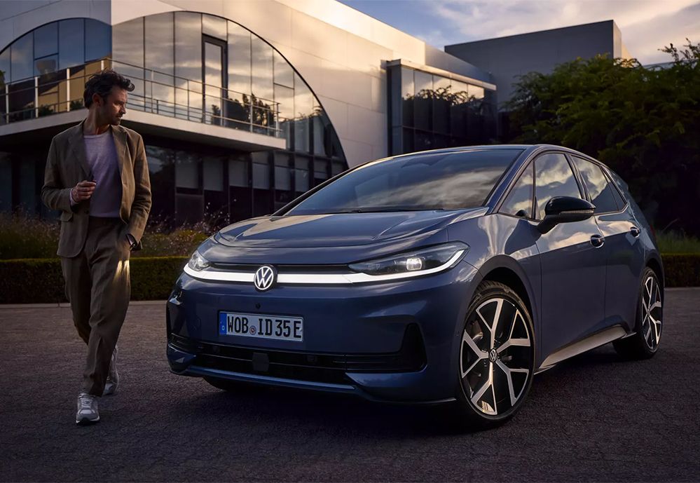 Blauer ID.3 Neo im Abendlicht mit erleuchtetem Frontlicht. Mann geht von links am Fahrzeug vorbei