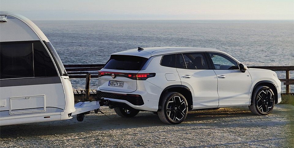 Volkswagen Tayron in Wei&szlig; mit Wohnwagen an Anh&auml;ngevorrichtung vor Meer