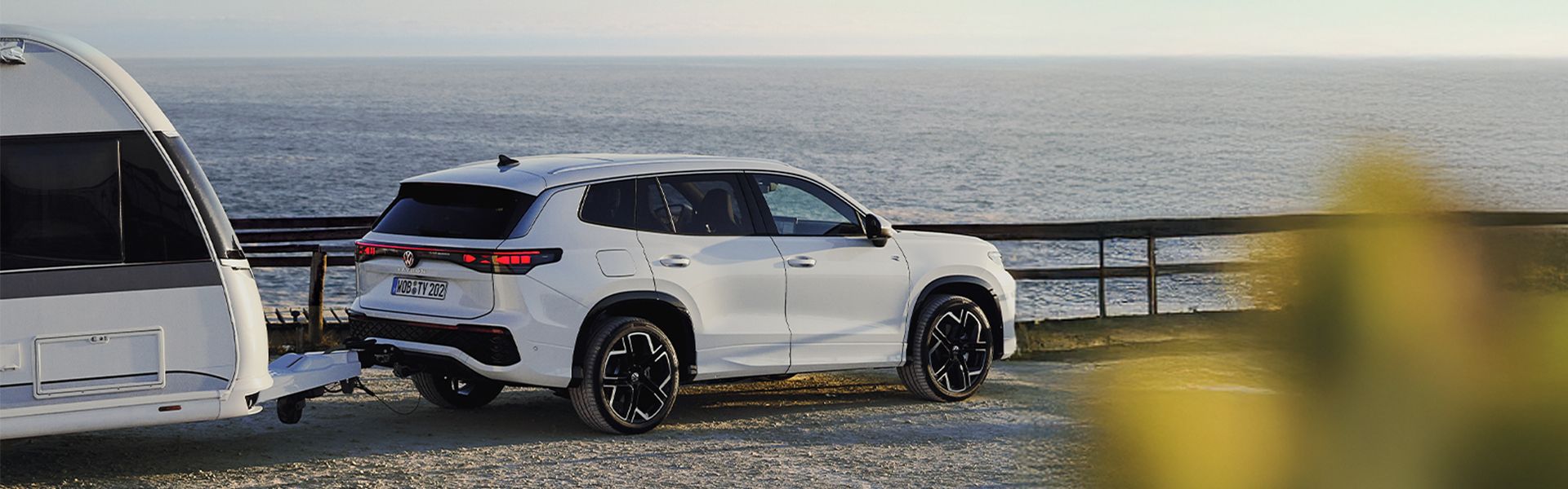 Volkswagen Tayron in Wei&szlig; mit Wohnwagen an Anh&auml;ngevorrichtung vor Meer